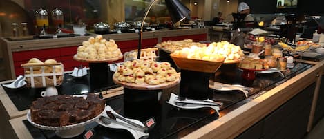 Un bufé con diversas opciones de comida, incluyendo pasteles, bollos y un pastel de chocolate.