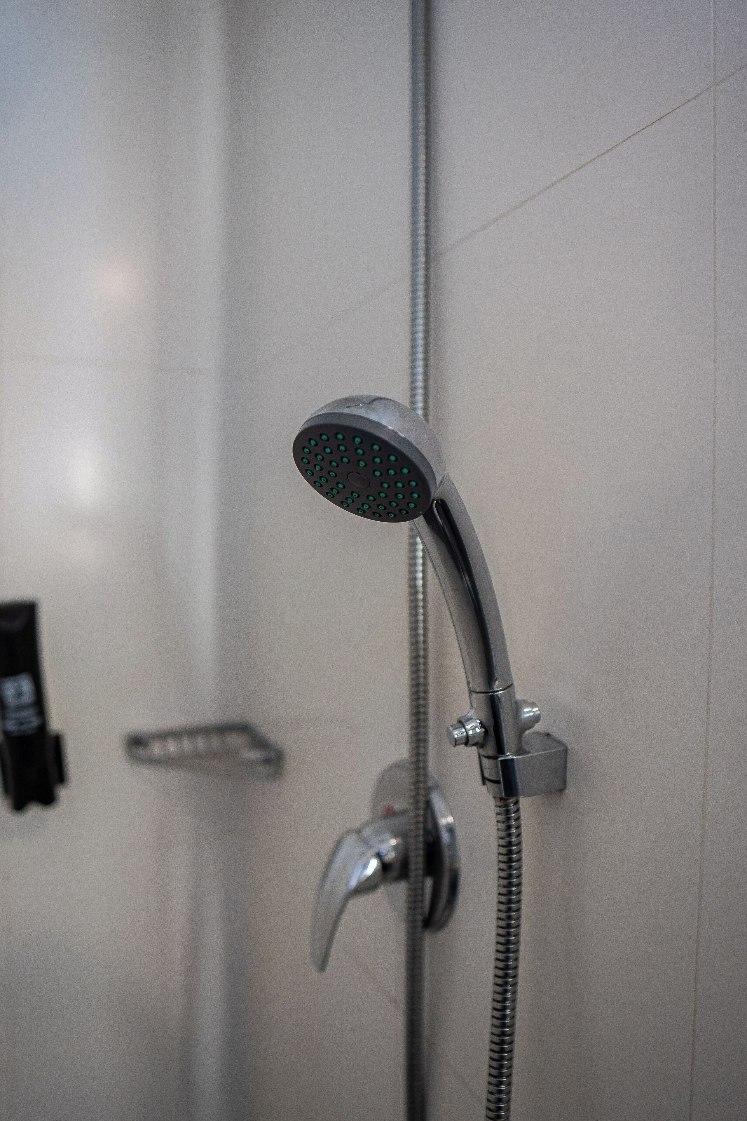A shower with a handheld showerhead and a wall-mounted control valve.