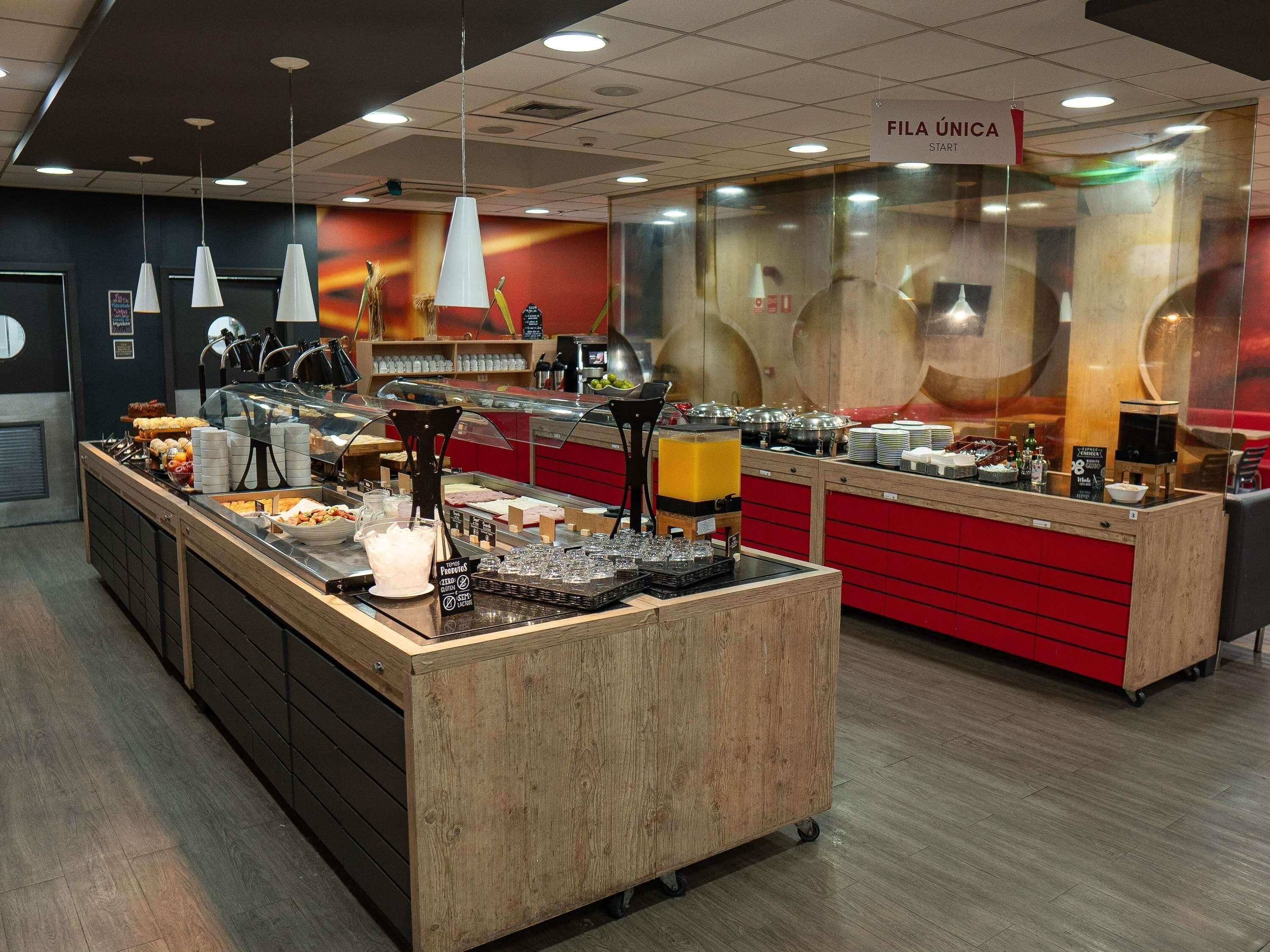 Un área de bufé con diversas opciones de comida, una estación de café y un cartel que indica FILA ÚNICA START.