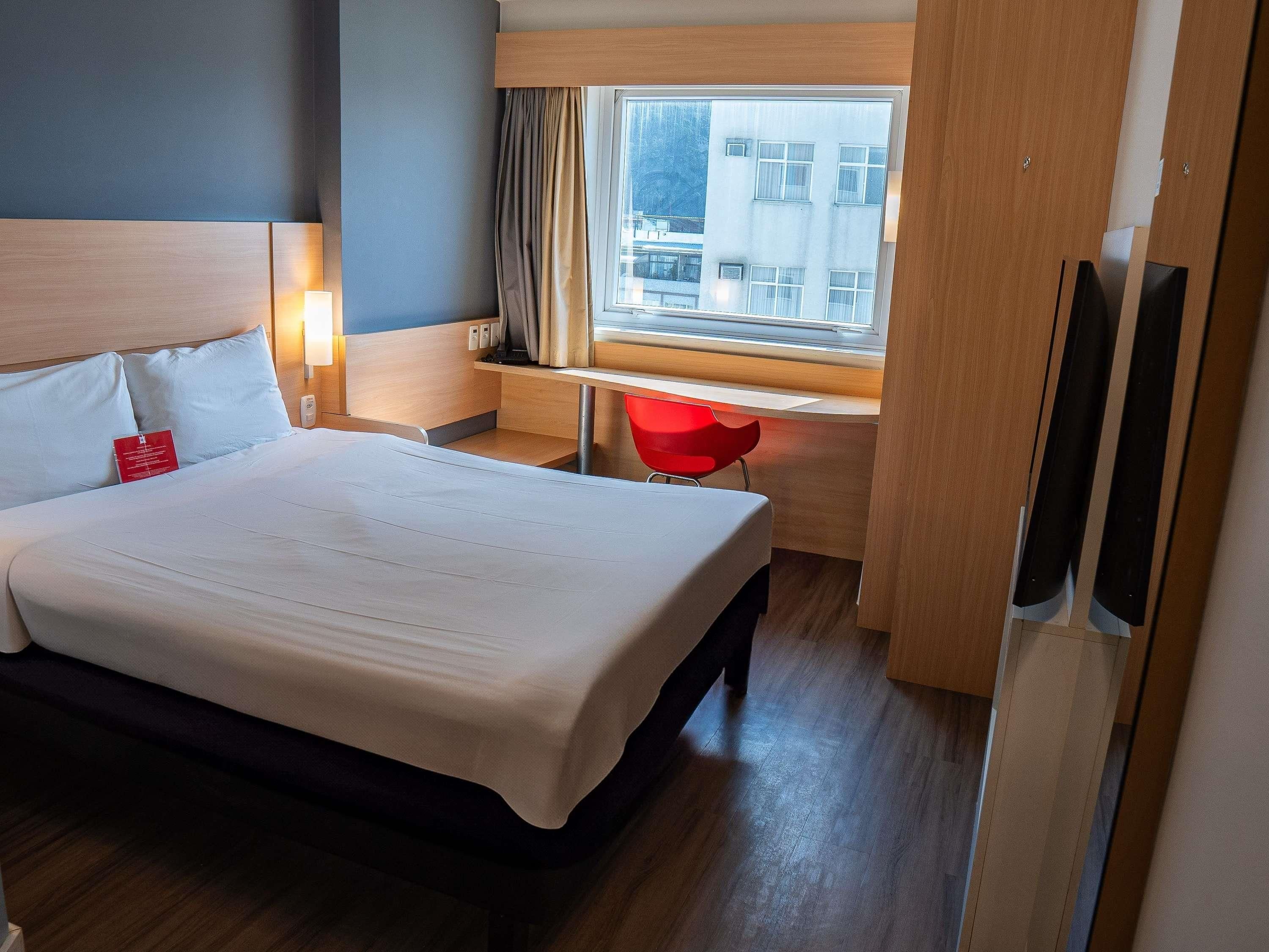 A hotel room with a bed, a desk, a chair, a window, and a TV.