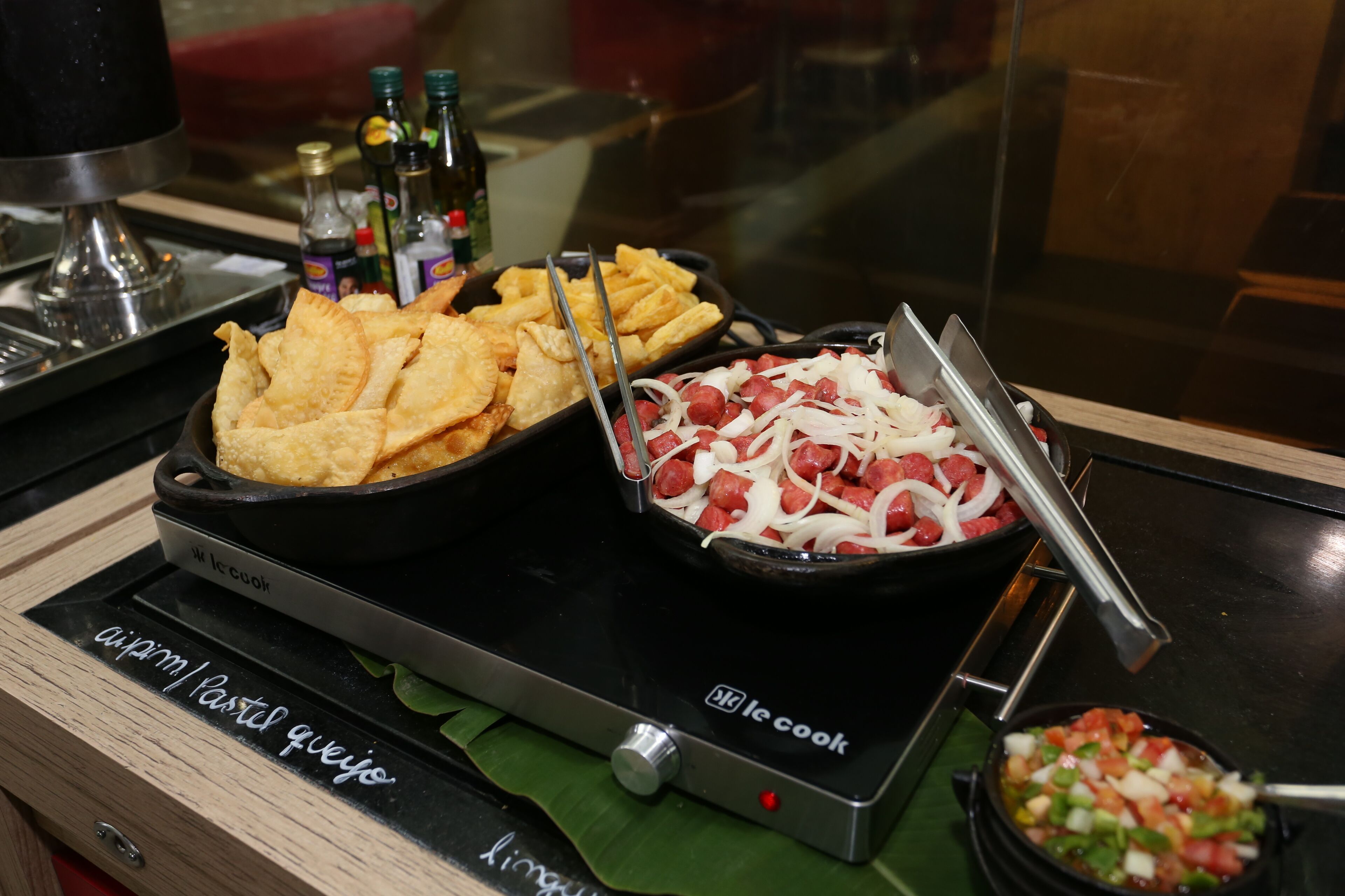 A kitchen counter with a black induction cooktop, a bowl of diced tomatoes, and a pan of sliced onions and sausages.