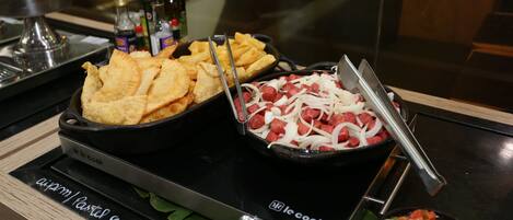 A kitchen counter with a black induction cooktop, a bowl of diced tomatoes, and a pan of sliced onions and sausages.
