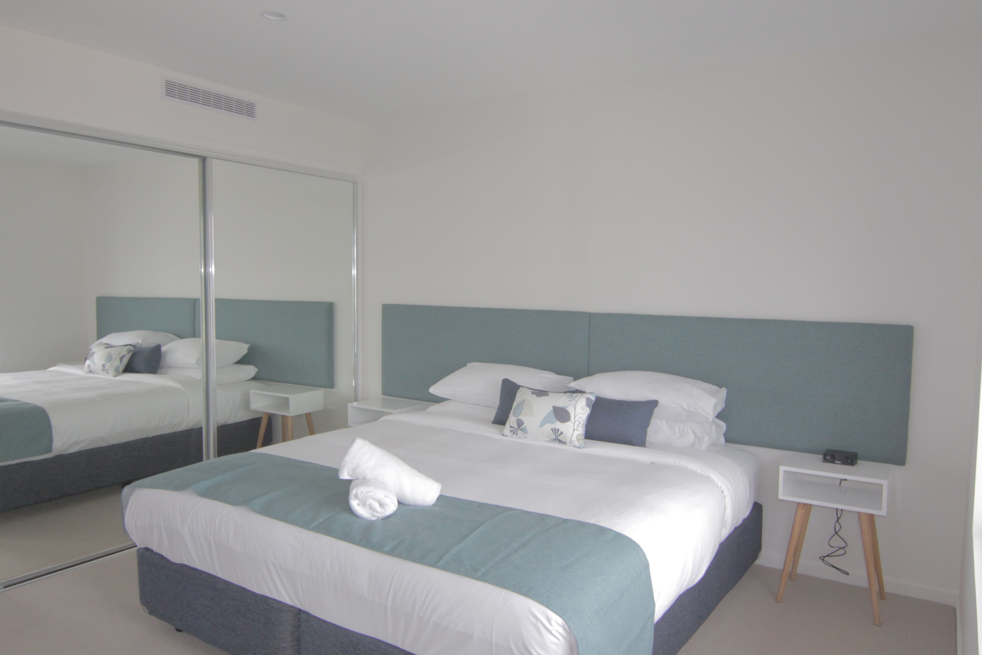 A modern hotel room with a large bed, a bedside table, a nightstand, a mirror, and a wall-mounted TV.