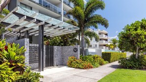A modern residential building with a covered entrance, a stone wall, and a well-maintained garden with various plants and flowers. - Verve on Cotton Tree (Maroochydore)