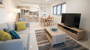 A modern living room with a sofa, TV, and dining area. - Verve on Cotton Tree (Maroochydore)
