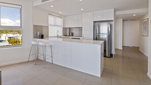 A modern kitchen with a central island, white cabinetry, and stainless steel appliances. - Verve on Cotton Tree (Maroochydore)