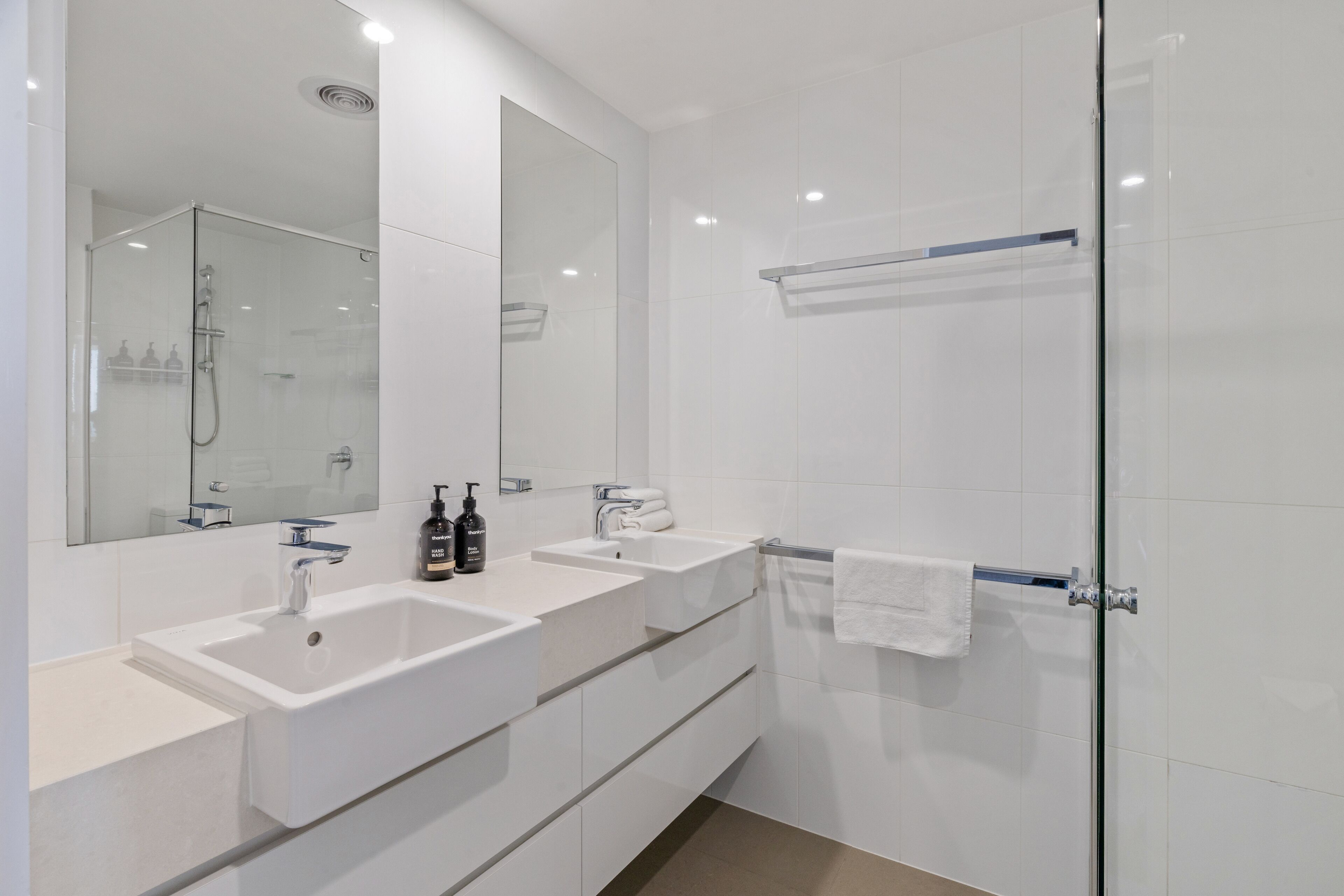 A modern bathroom with two sinks, a glass shower enclosure, and a large mirror.