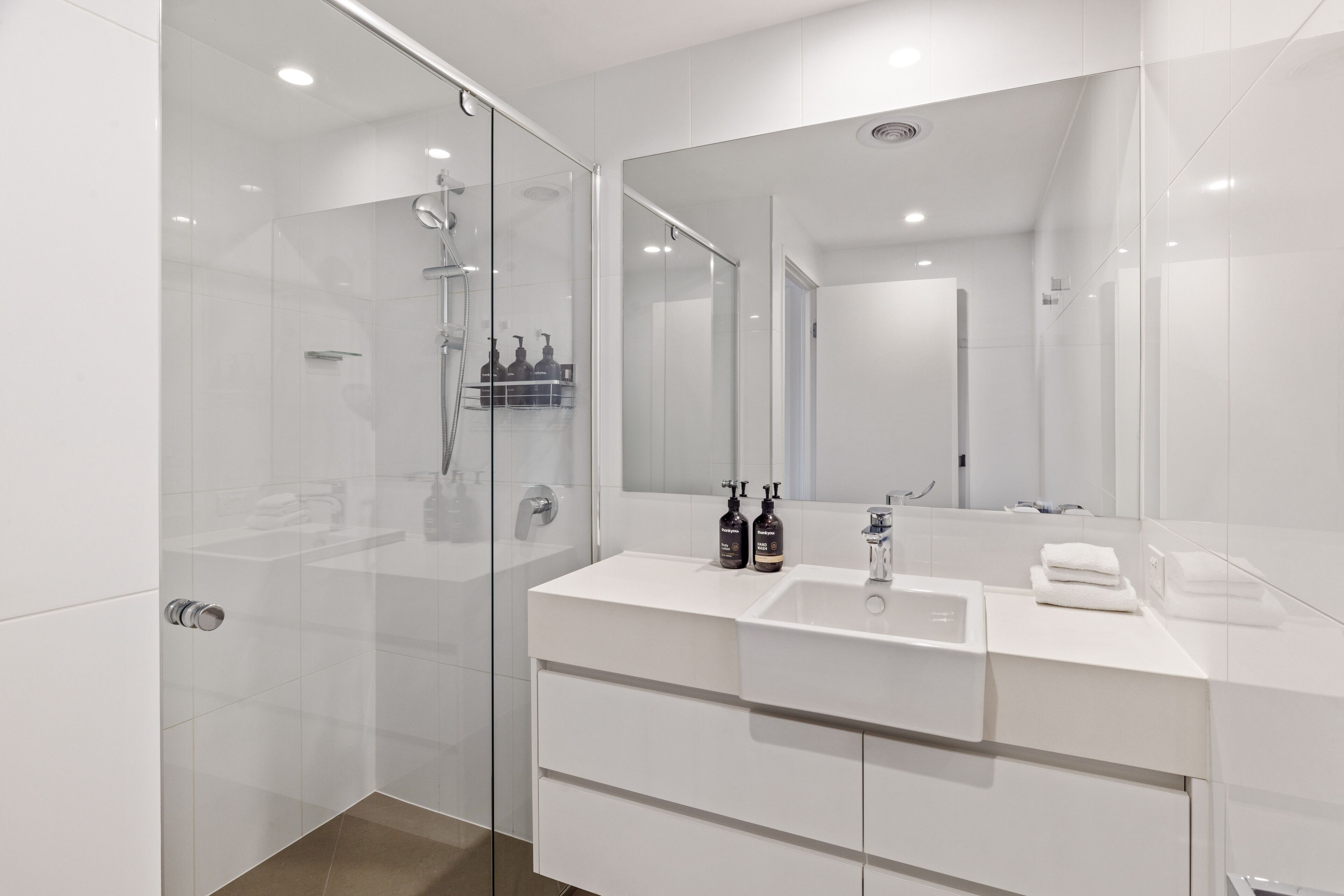 Un baño moderno con ducha de vidrio, tocador blanco con lavamanos y un espejo grande.