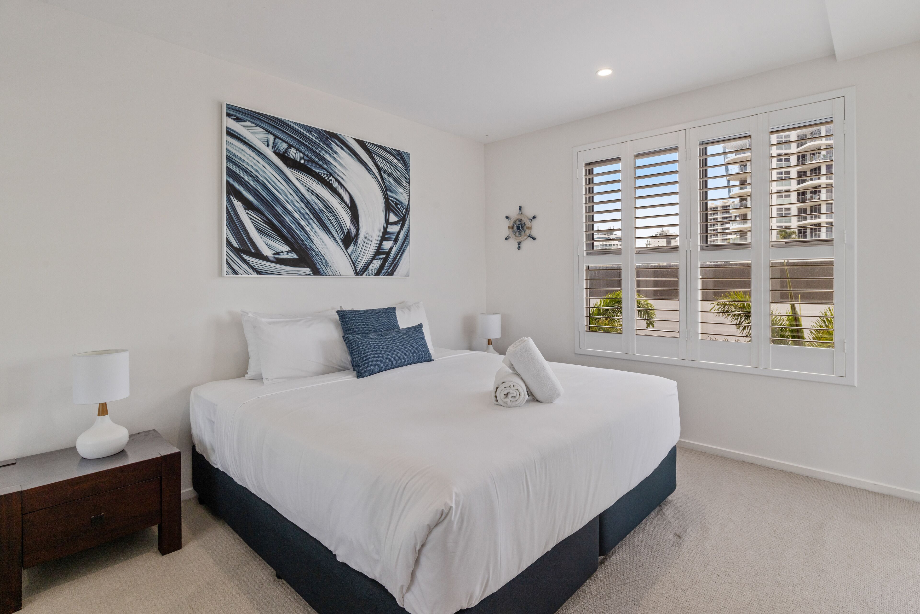 Une chambre à coucher moderne avec un grand lit, une table de chevet, une horloge murale et une fenêtre avec des stores.