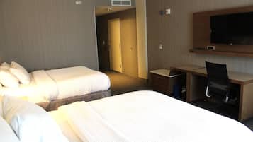 A hotel room with two beds, a desk, a chair, a television, and a door leading to another room.