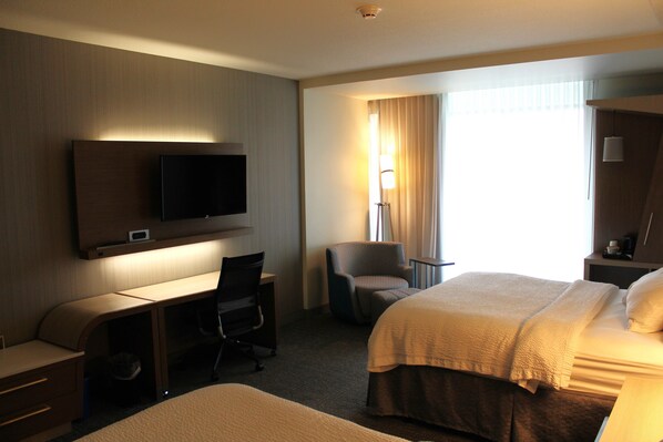 Habitación de hotel con cama, escritorio, silla, televisor y lámpara.