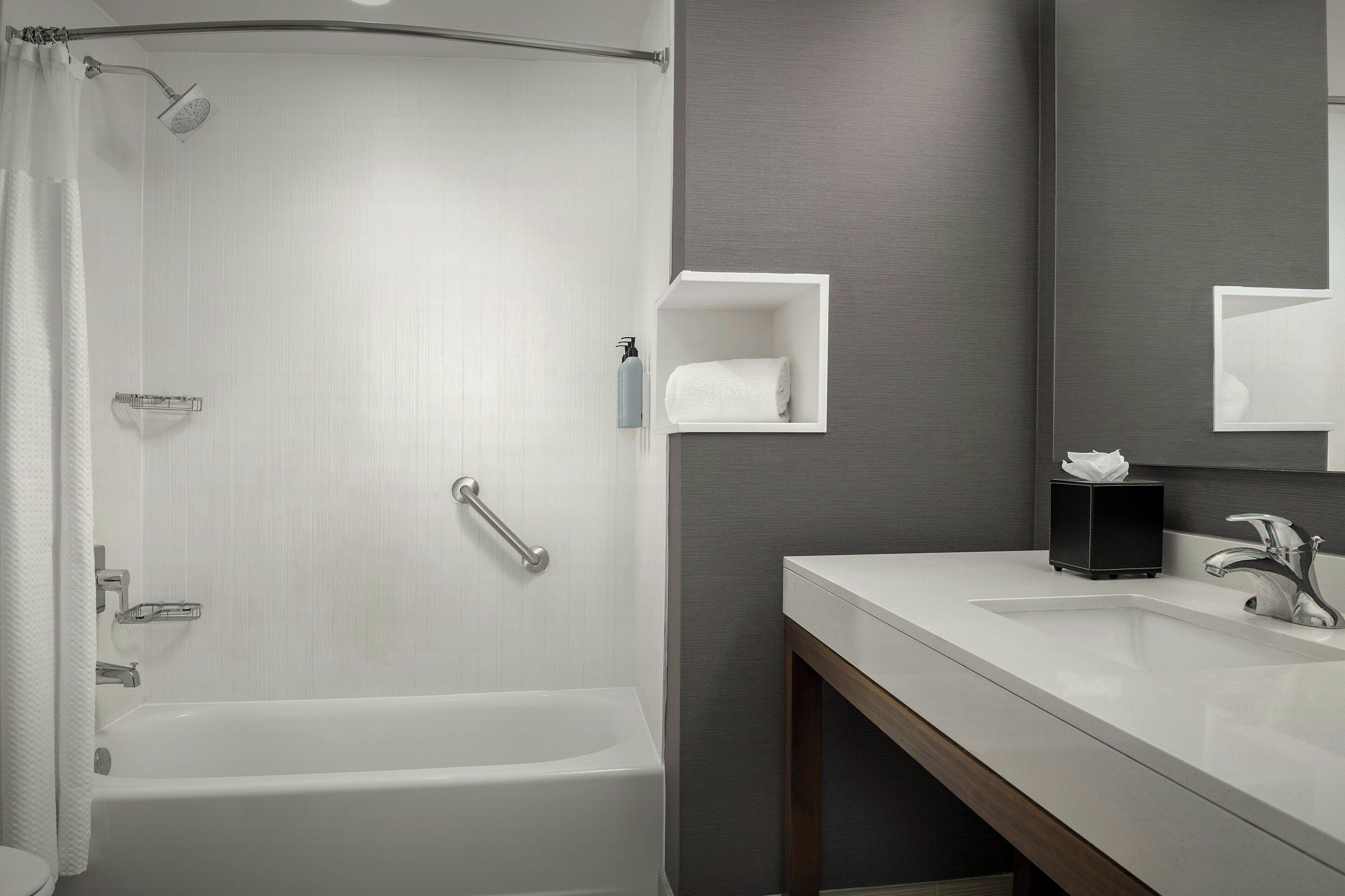 Une salle de bain moderne avec une baignoire, un lavabo blanc, un miroir et un porte-serviettes.