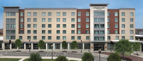 A Courtyard hotel with a modern design, featuring a central courtyard with trees and a fountain, and a ground floor with retail spaces.