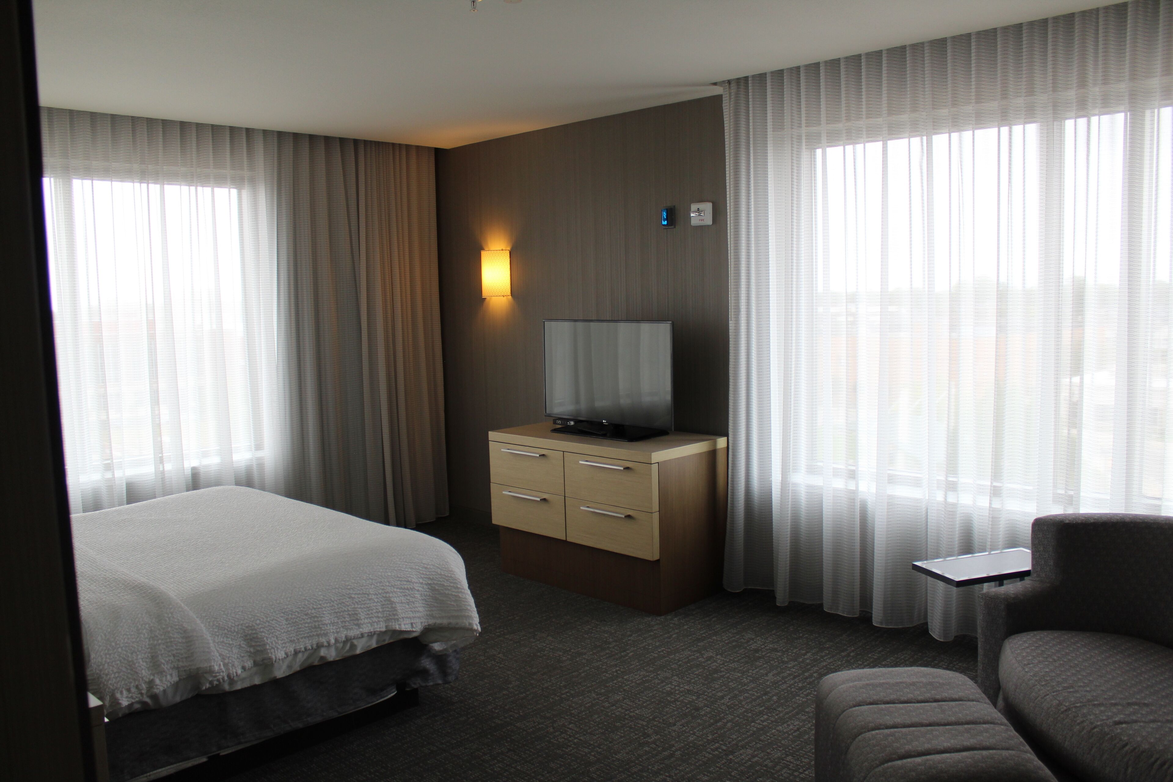 A hotel room with a bed, a desk with a television, and a chair.