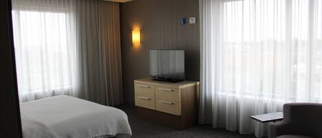 A hotel room with a bed, a desk with a television, and a chair.