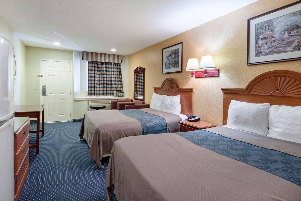 Quarto de hotel com duas camas, uma mesa, uma cadeira, um espelho e uma janela com cortinas.