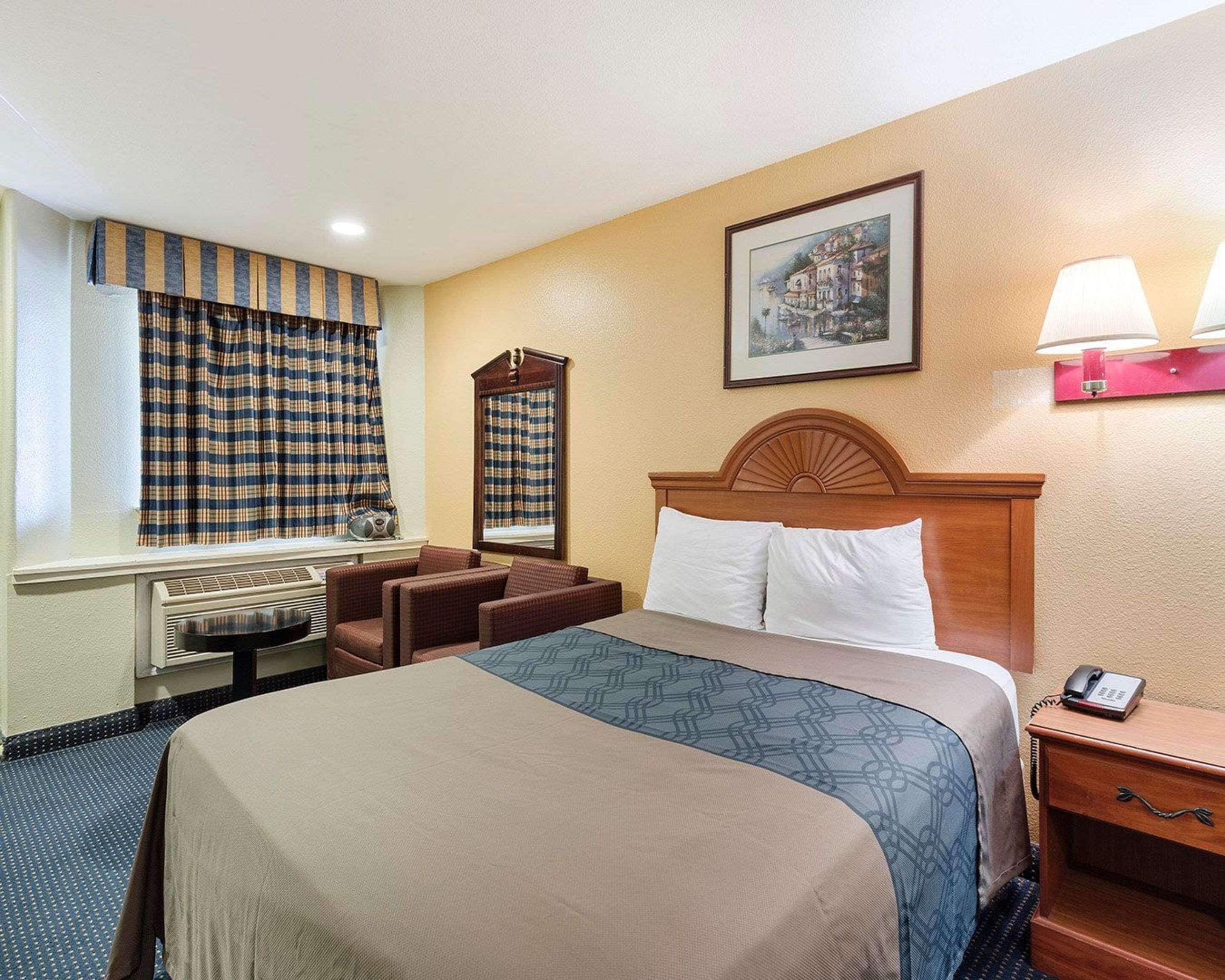 Habitación de hotel con cama, escritorio, silla, lámpara, teléfono y un cuadro en la pared.