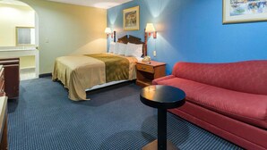 Quarto de hotel com cama, sofá vermelho, mesinha e um quadro na parede.