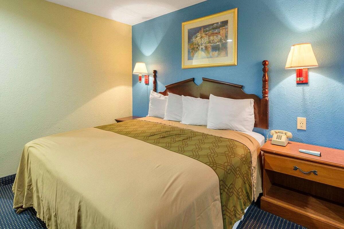 Quarto de hotel com cama, luminárias de cabeceira, mesa de cabeceira, telefone e um quadro na parede.