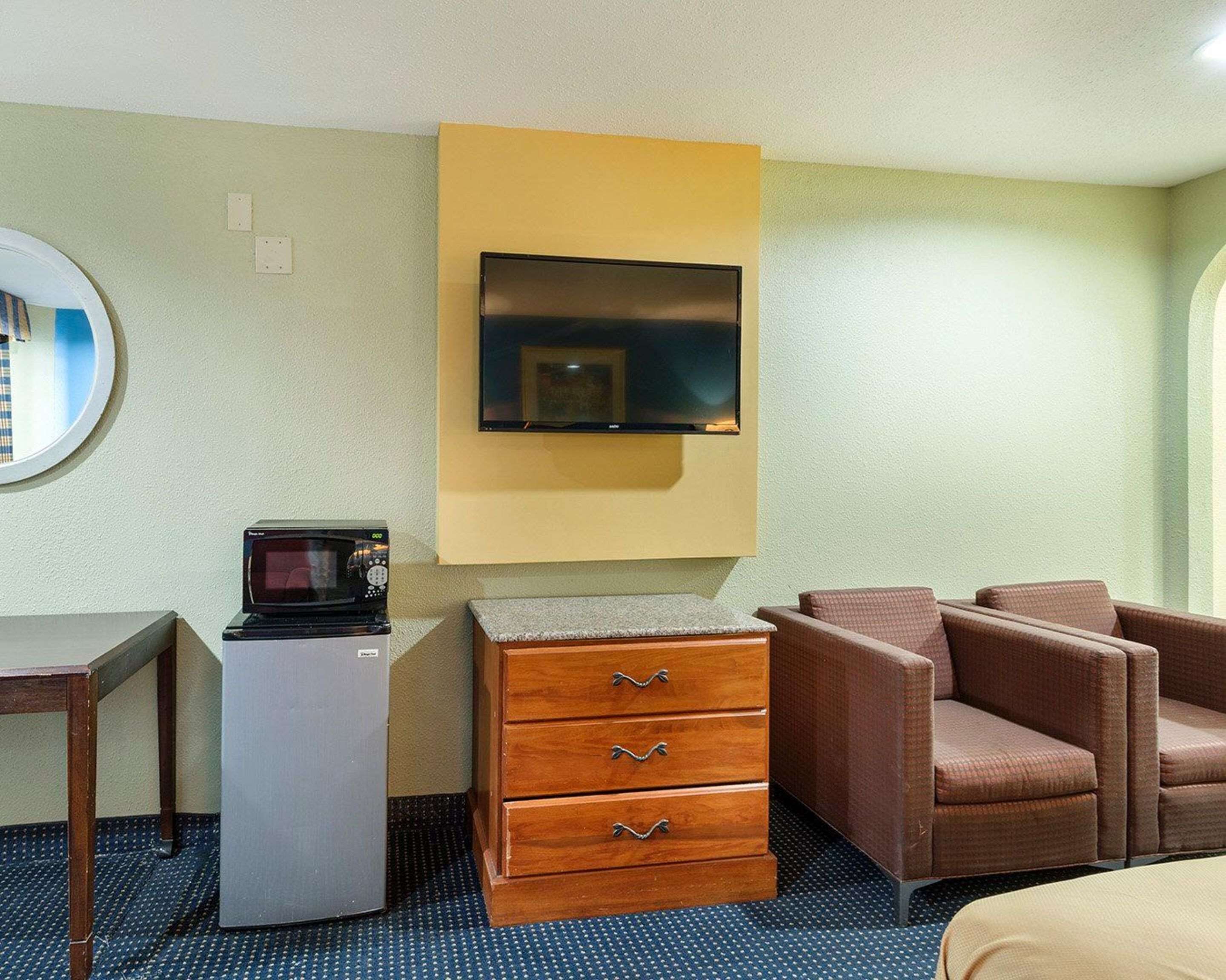 Ein Hotelzimmer mit Schreibtisch, Mikrowelle, Kommode, Fernseher und zwei Sesseln.