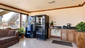 Quarto de hotel com sofá, cozinha compacta, máquina de vendas automática e vista para o exterior.