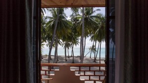 Vista a la playa desde una habitación con techo de madera, una mesa roja y sillas blancas con cojines.