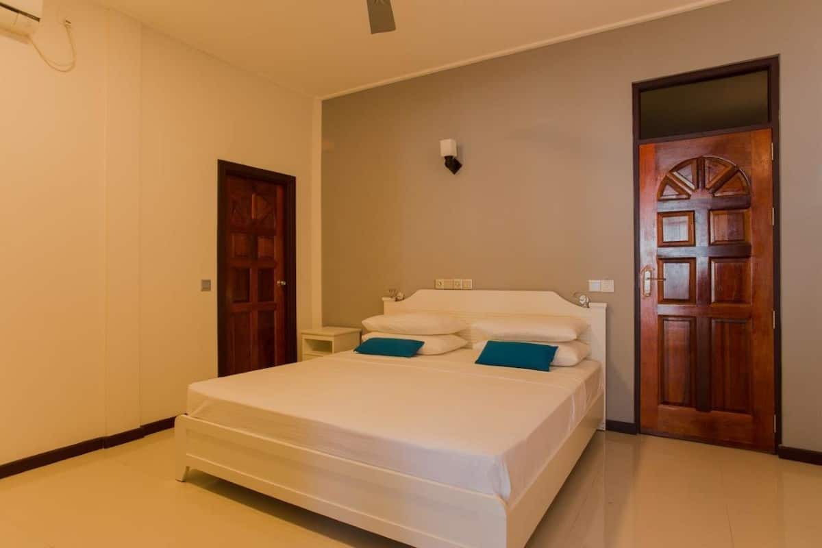 A bedroom with a single bed, a nightstand, a wall-mounted light, and two wooden doors.