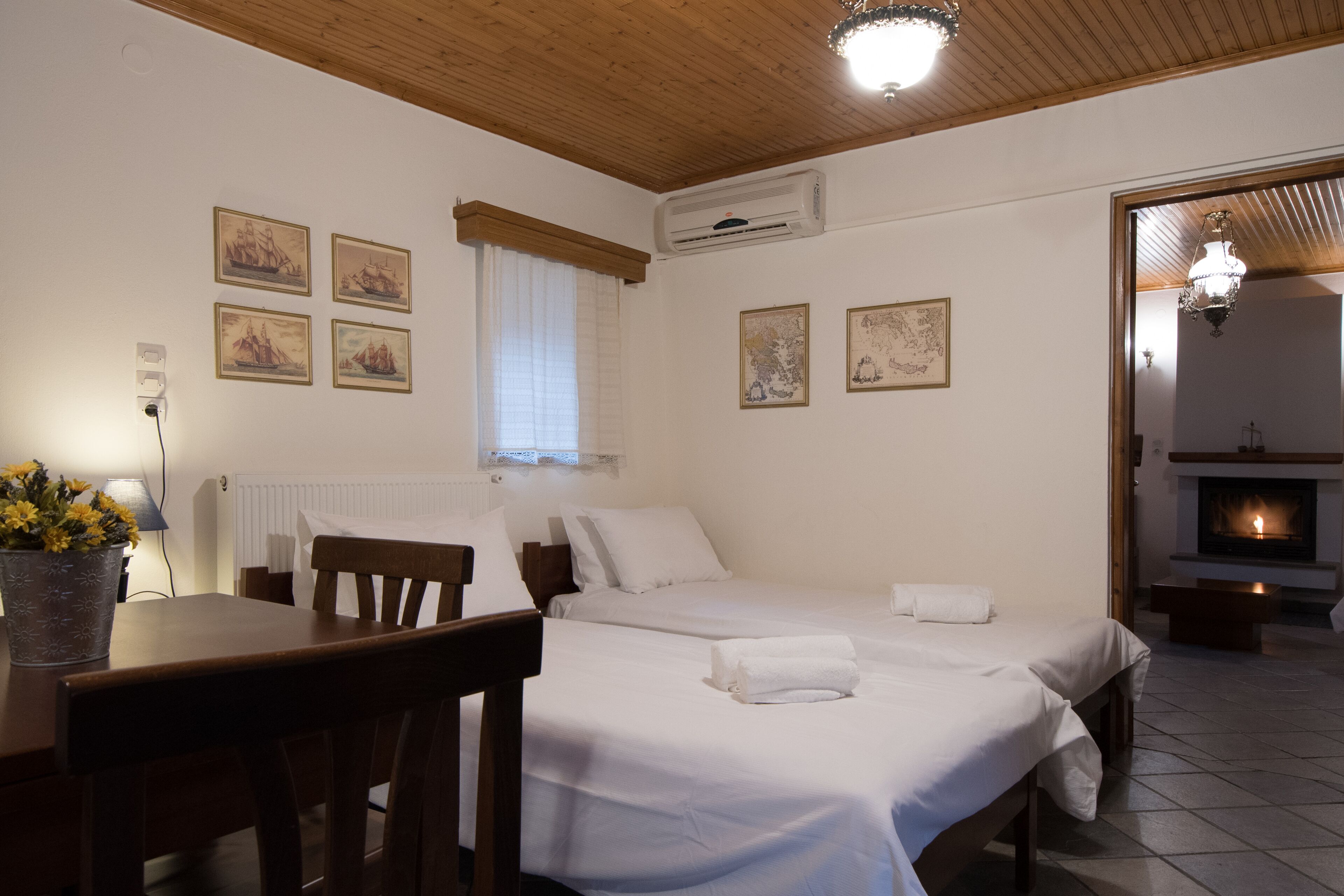 A room with two beds, a wooden ceiling, a radiator, a table with a potted plant, and a fireplace.