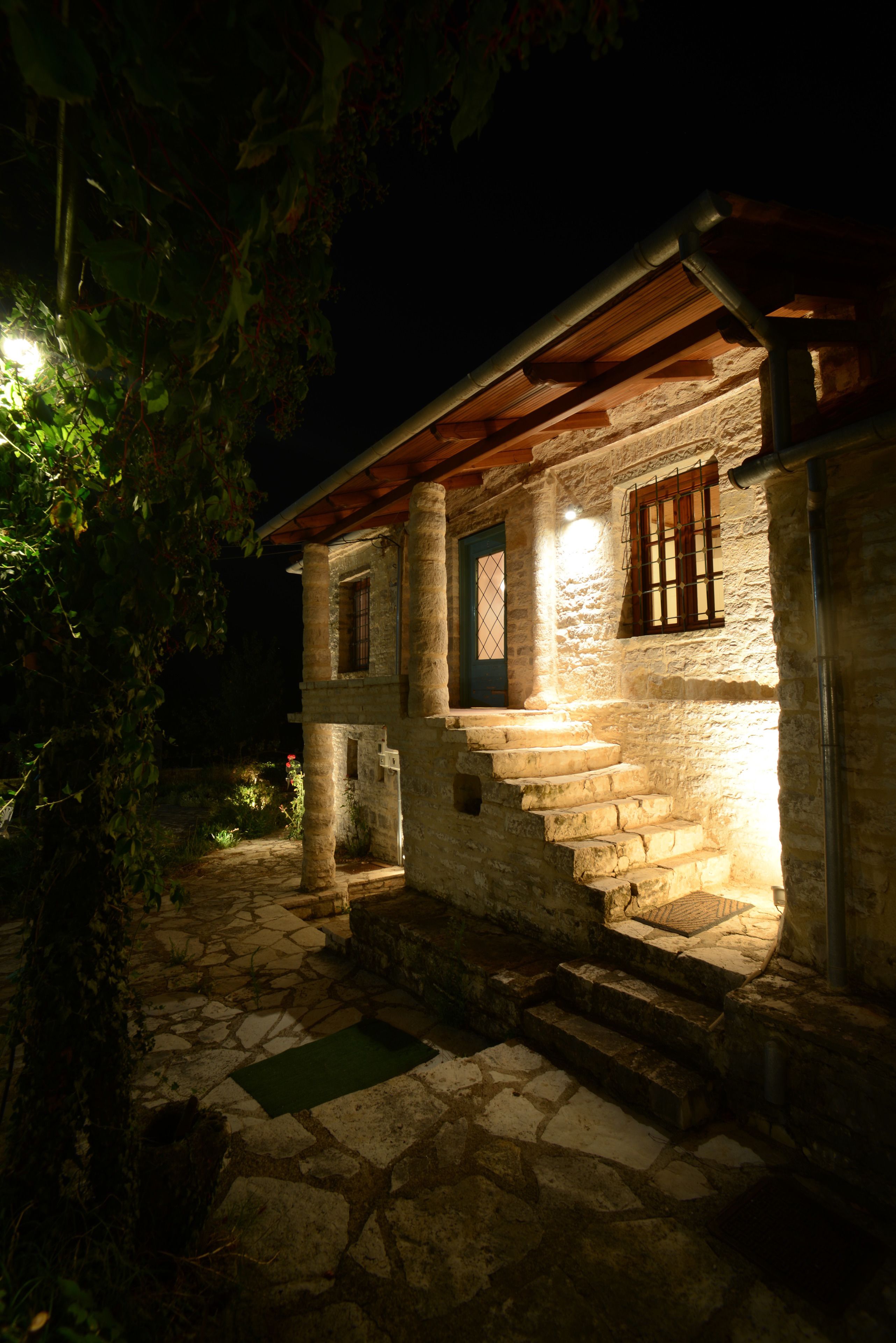 A stone building with a wooden staircase leading to a door, surrounded by foliage.