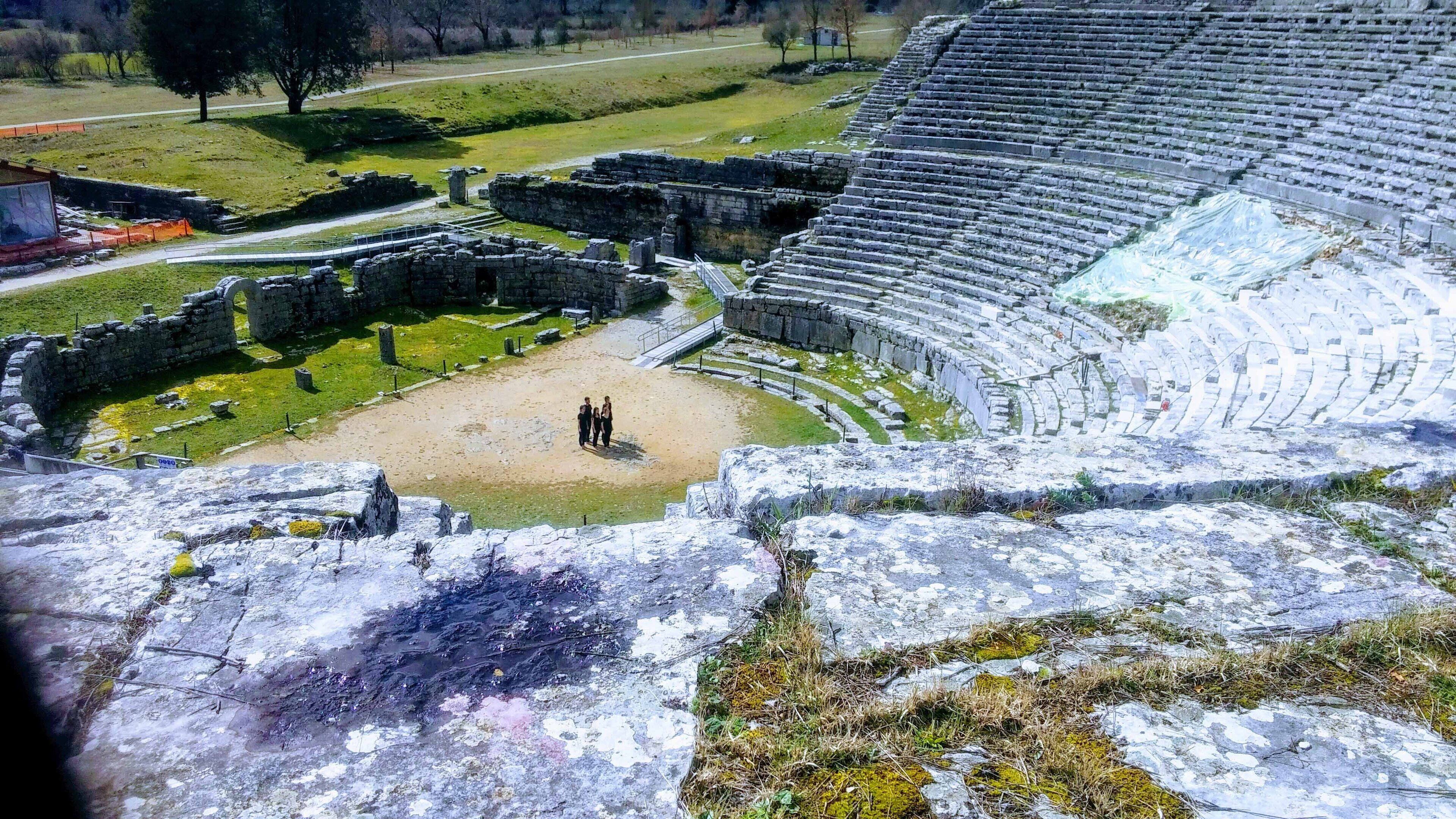 An ancient amphitheater with stone seating and a central stage area.