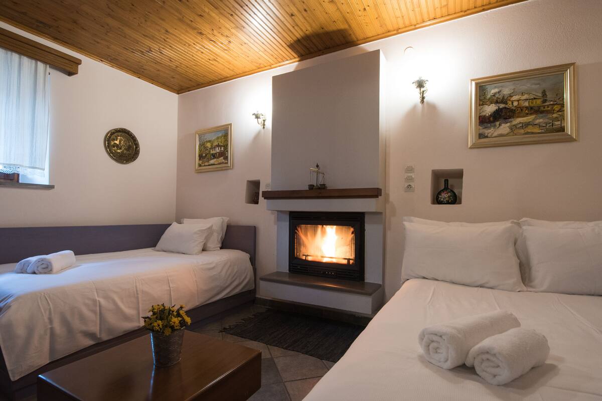 A hotel room with two beds, a fireplace, a wooden ceiling, and artwork on the walls.