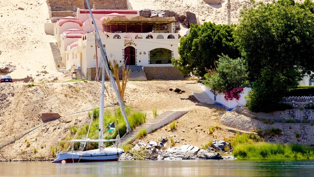 A traditional building with a staircase leading up to a door, situated near a body of water with a sailboat docked nearby. - Hadouta Masreya - Nubian Guest House (Aswan)