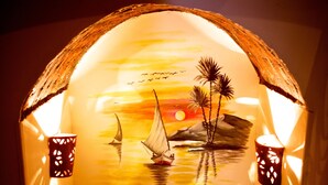 A cozy room with a wooden floor, a small round table, and a mural of a sunset scene with a sailboat. - Hadouta Masreya - Nubian Guest House (Aswan)