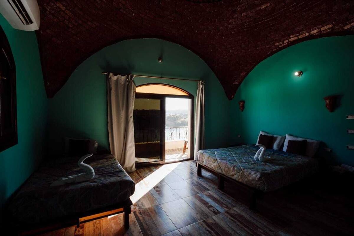 Une chambre avec deux lits, une grande porte en arc et une vue sur l’extérieur.