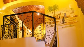 A staircase with a wrought iron railing, a small table, and a mural of a sunset scene. - Hadouta Masreya - Nubian Guest House (Aswan)