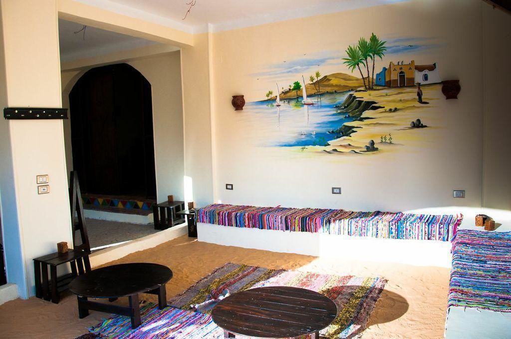 A room with a large bed, a chair, a small table, a colorful rug, and a mural of a beach scene on the wall.