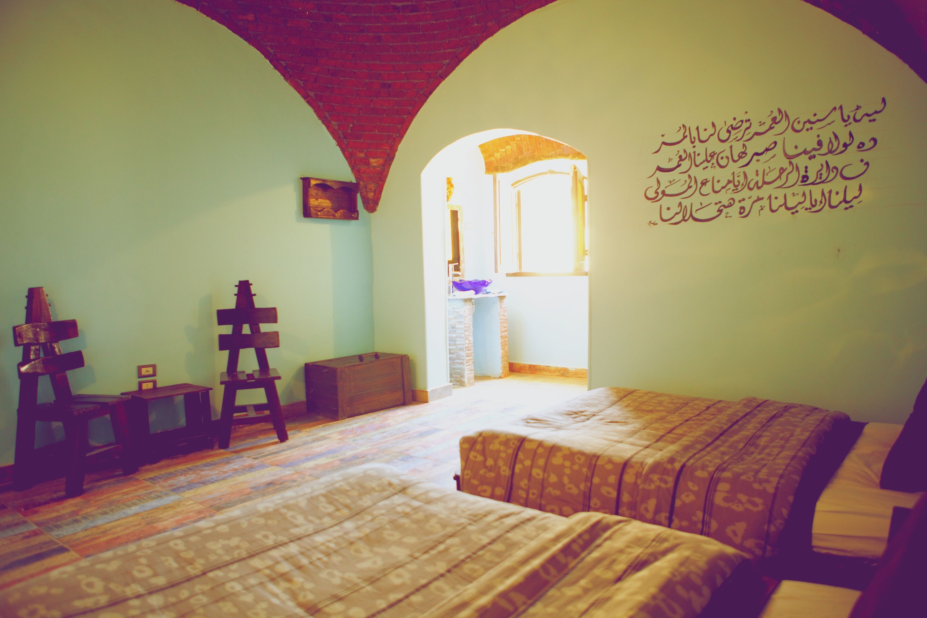 Een kamer met een bed, een houten stoel, een kleine tafel en een muur met Arabische tekst.