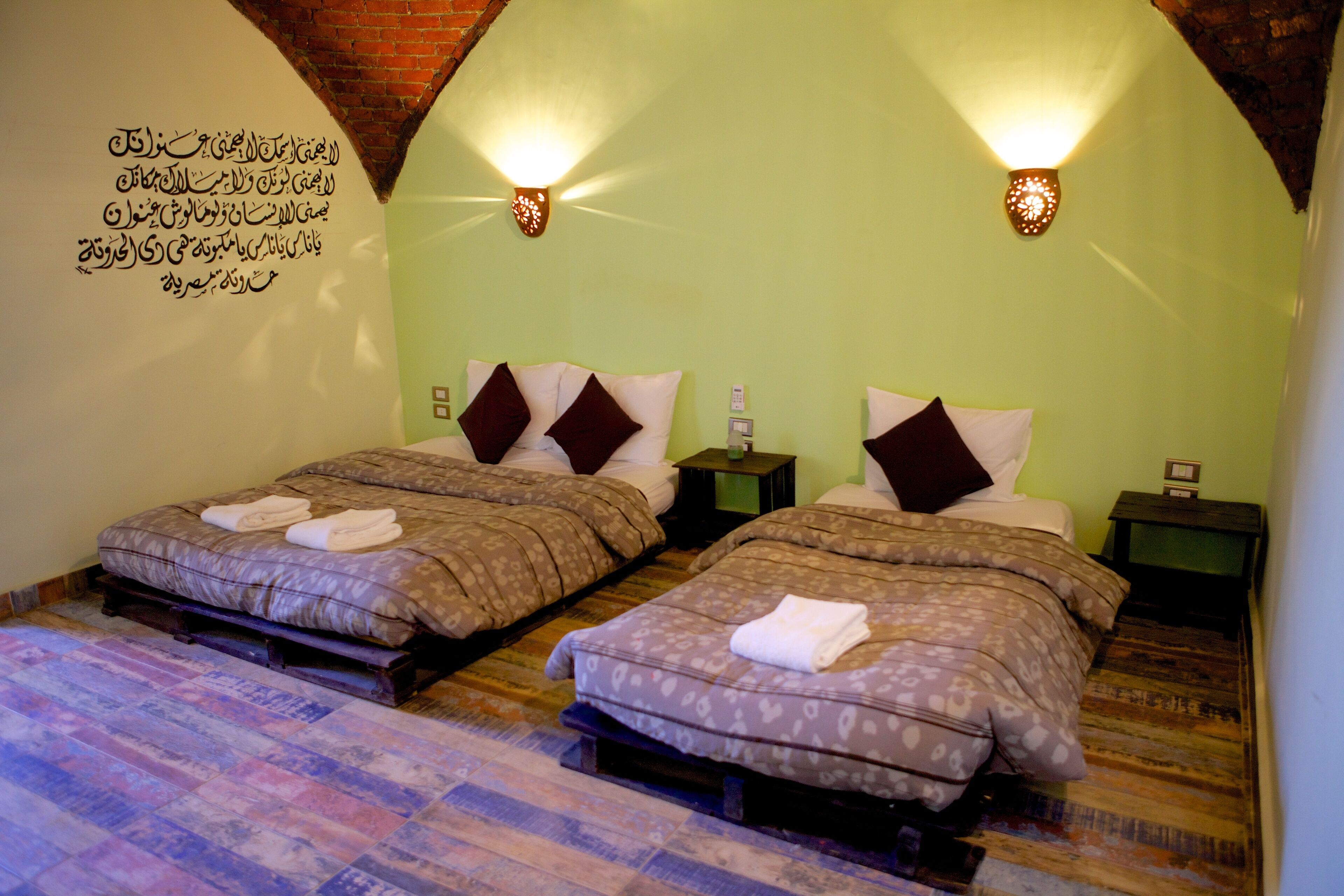 A room with two beds, each with a pillow and a small nightstand.