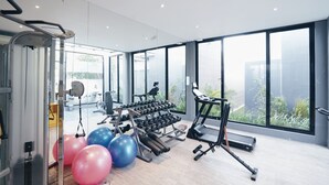 A modern gym with exercise equipment, large windows, and a view of greenery. - Kamaniiya Petitenget Seminyak (Keroboken Kelod)