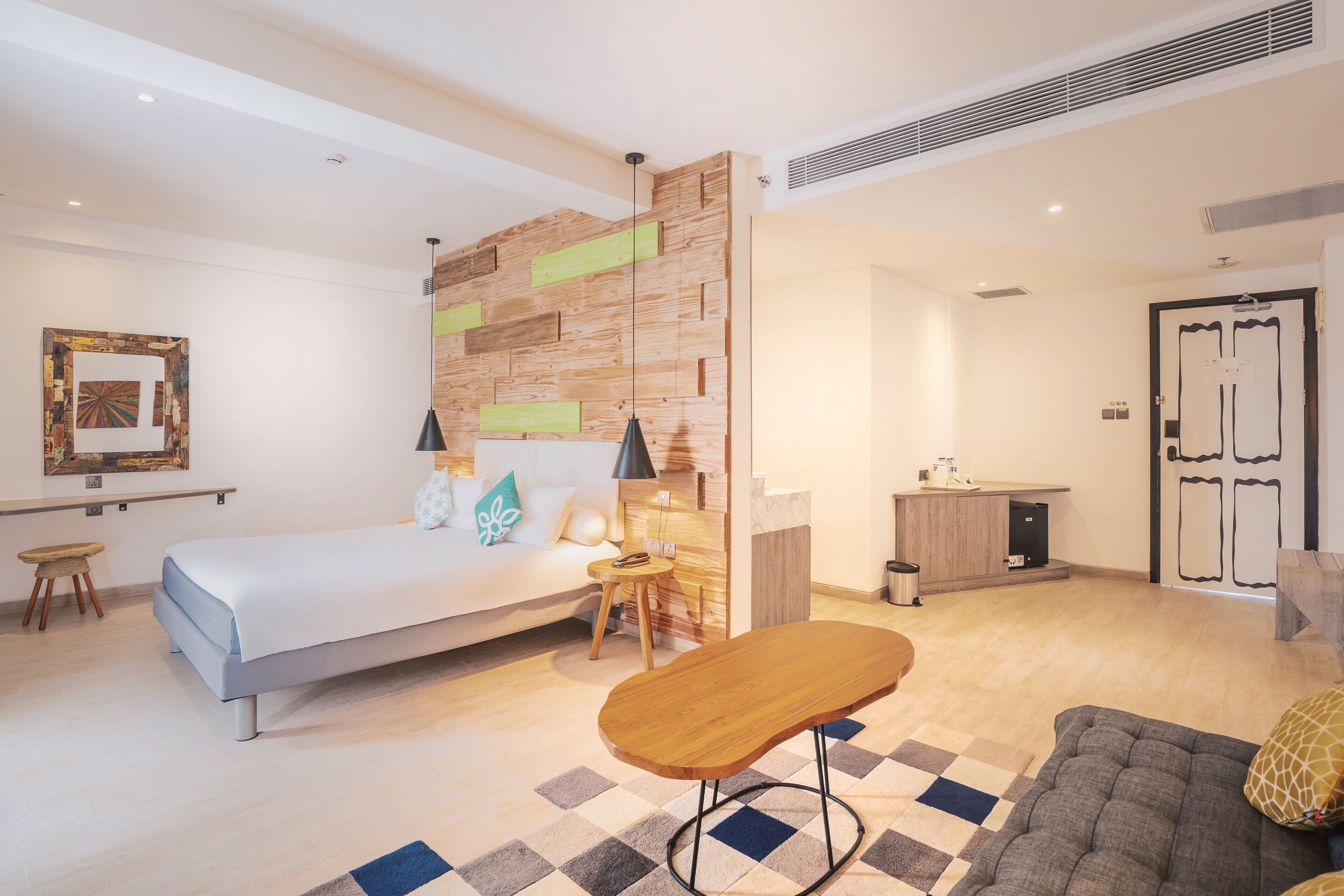 Et moderne hotelværelse med seng, lille bord, sofa, en væg med trædetaljer og et tekøkken.
