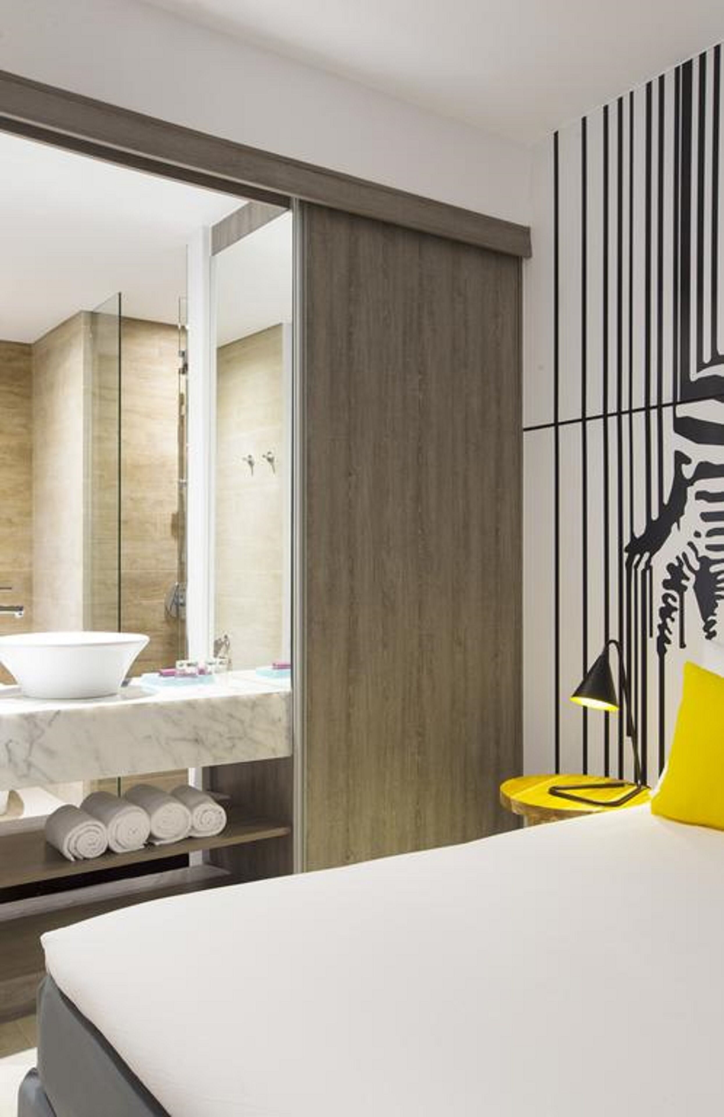 A modern hotel room with a large bed, a bathroom with a marble sink, and a zebra mural on the wall.