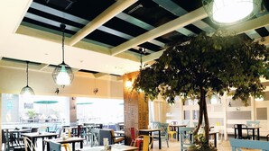 A spacious indoor area with tables and chairs, a large tree, and hanging light fixtures. - Kamaniiya Petitenget Seminyak (Keroboken Kelod)