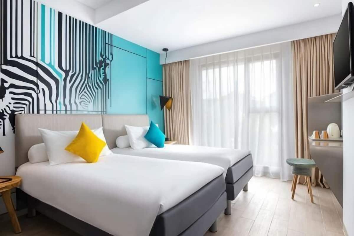 Ein Hotelzimmer mit zwei Betten, einem Fernseher, einem Schreibtisch und einer Wandmalerei mit Zebra-Motiv.