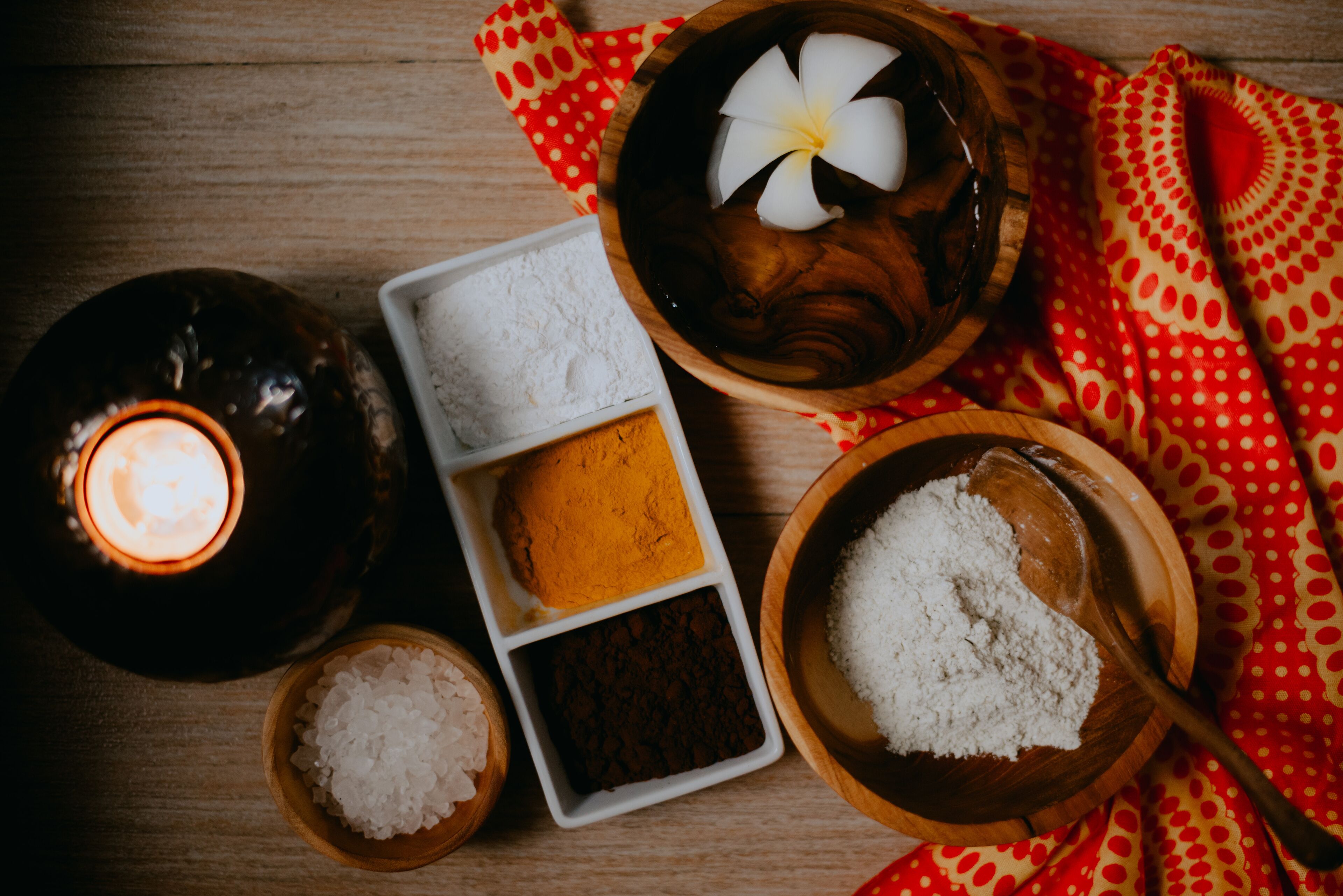 A wooden table with a lit candle, a bowl of white salt, a wooden spoon, and a small bowl of brown powder.