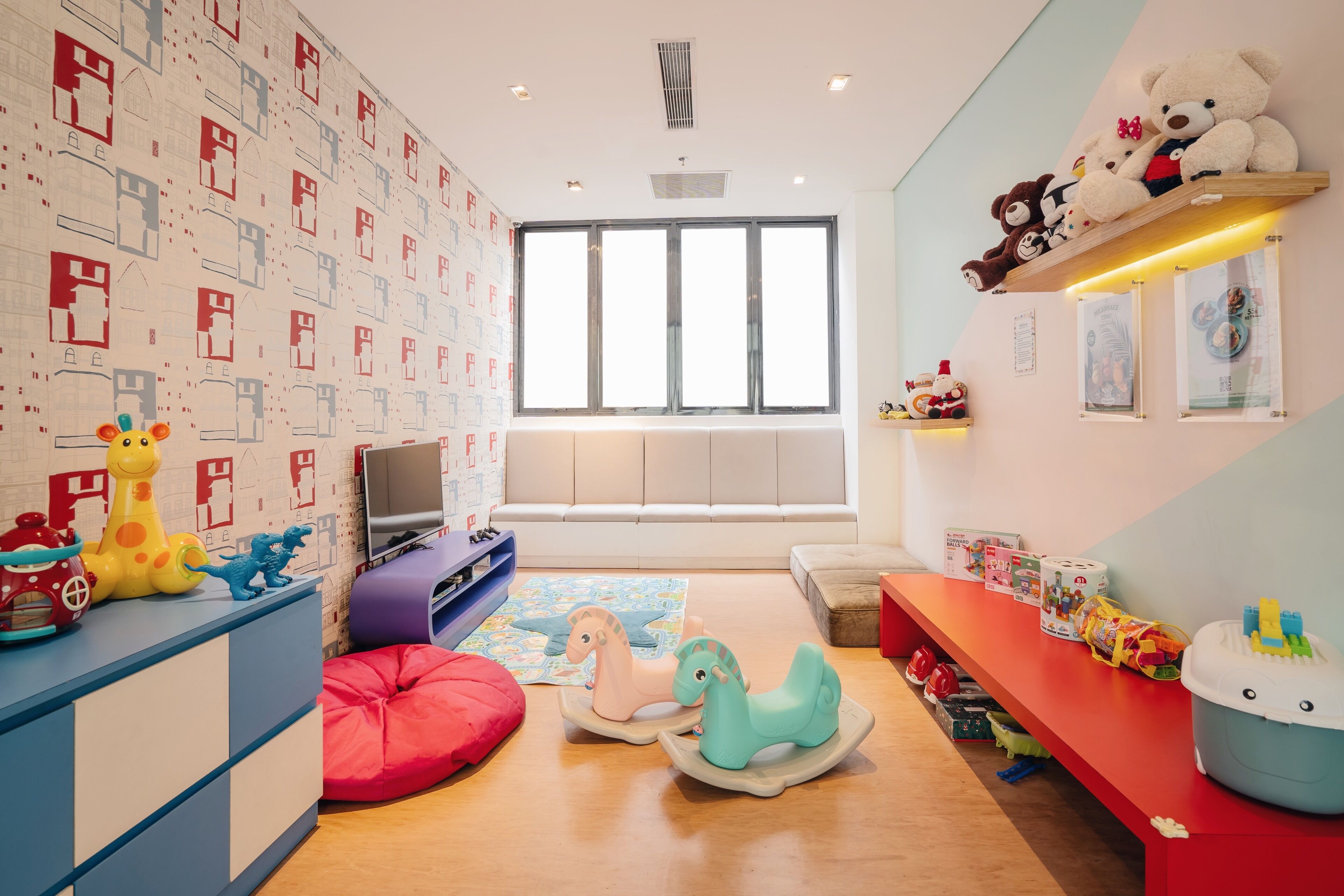 Une salle de jeux pour enfants avec une grande fenêtre, un téléviseur et divers jouets.