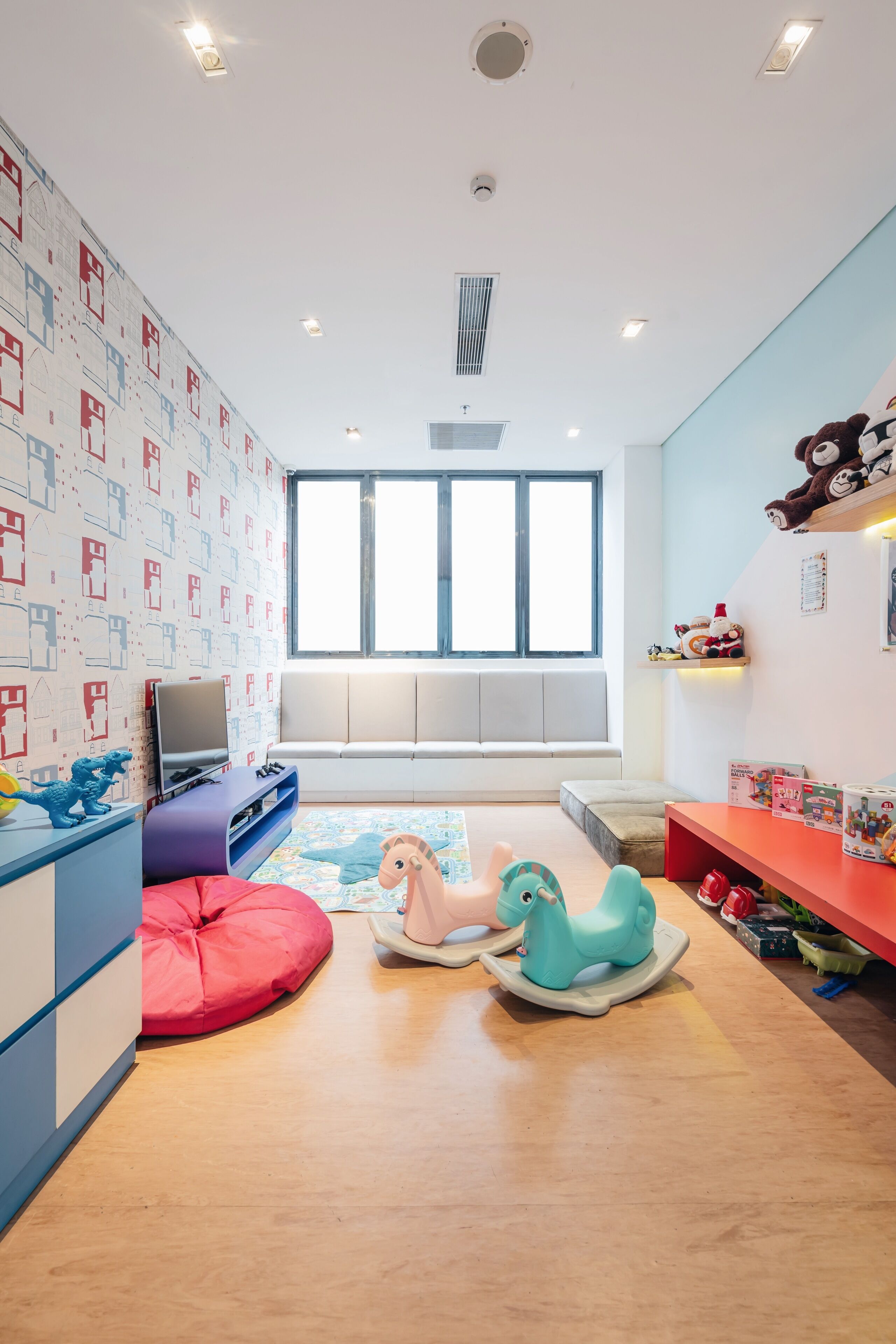 Una stanza giochi per bambini con una grande finestra, un divano, una televisione e diversi giocattoli.
