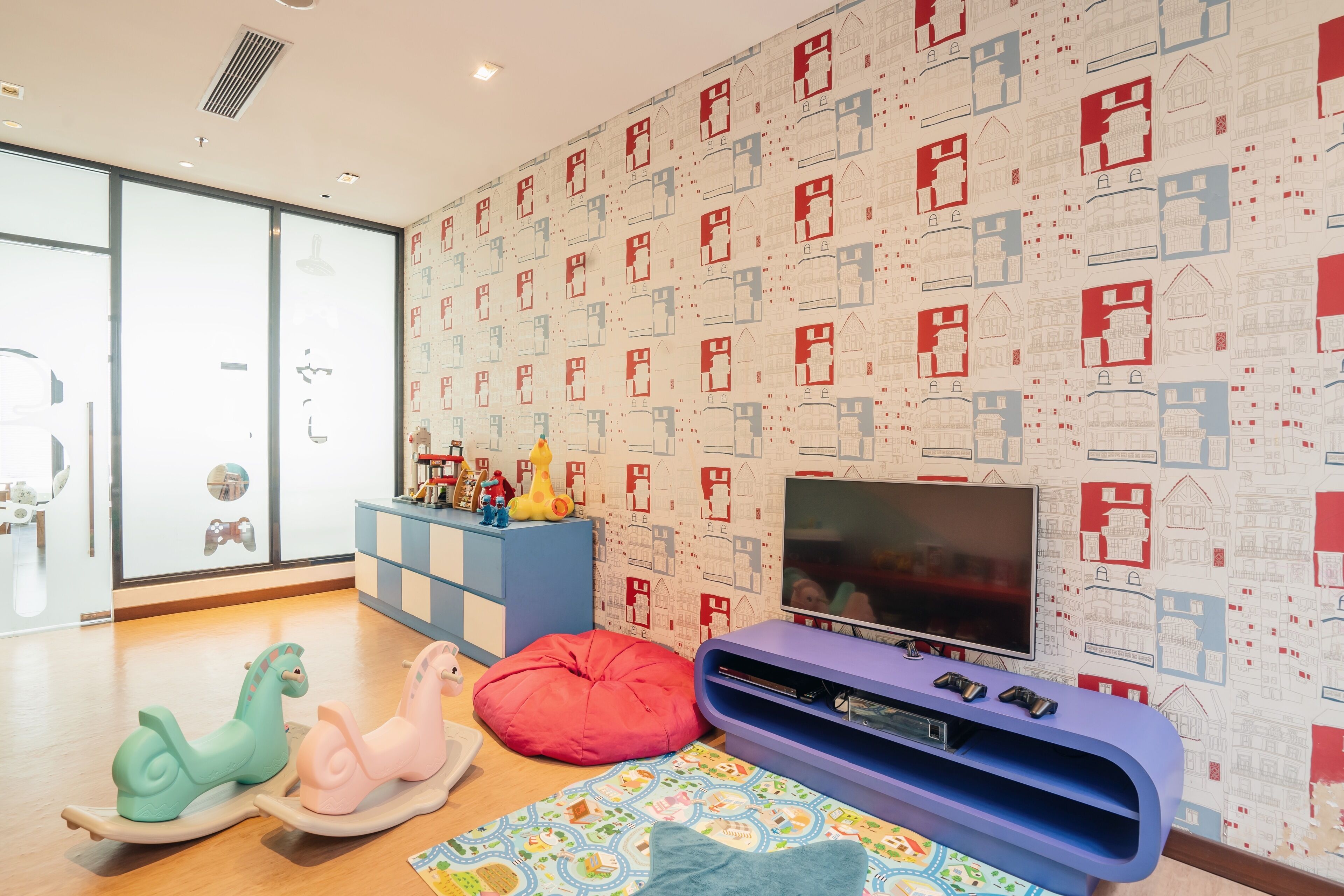 Ein Kinderspielbereich mit Fernseher, Schaukelpferden und einer Wand mit Muster.