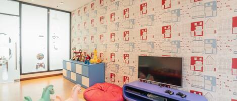 Ein Kinderspielbereich mit Fernseher, Schaukelpferden und einer Wand mit Muster.