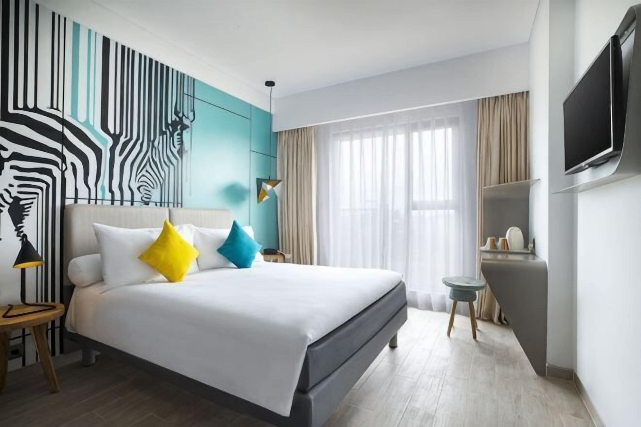 A modern hotel room with a large bed, a TV, a small table, and a zebra-patterned wall.