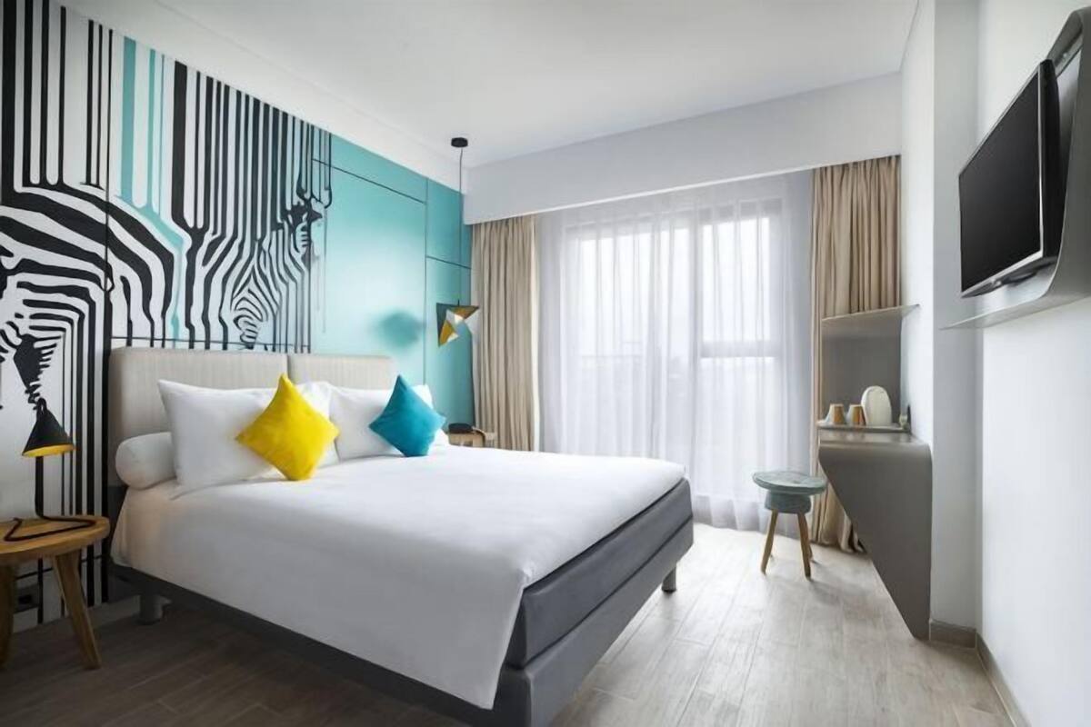 Ein modernes Hotelzimmer mit einem großen Bett, einem Fernseher, einem kleinen Tisch und einer Wand mit Zeprazmuster.